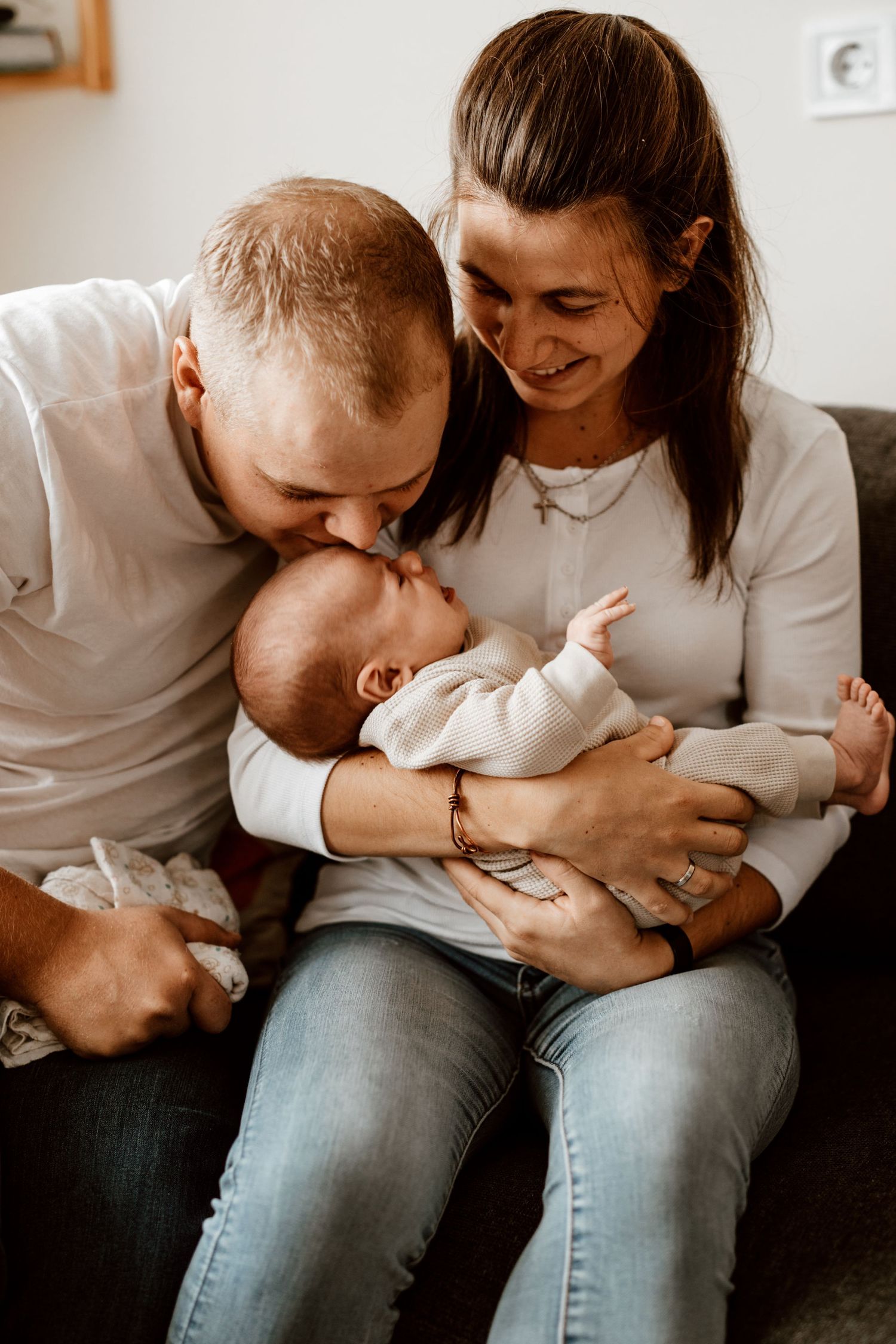 An intimate family moment as parents share affection with their baby on a couch.