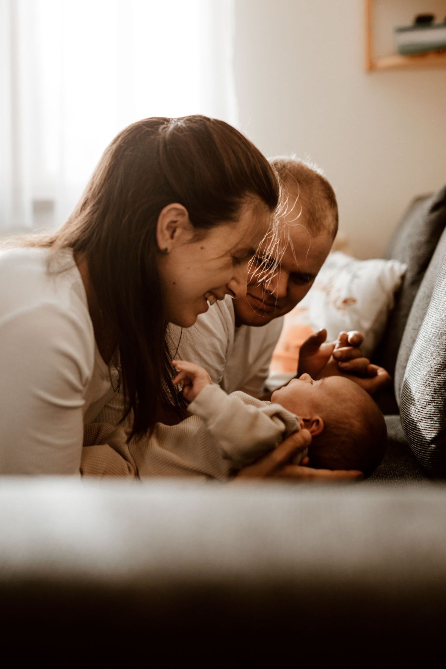 Intimate family moment with parents gazing adoringly at their baby on the couch.