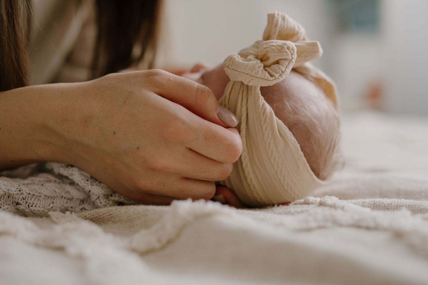 Close-up of hands adjusting delicate fabric wrap on textured bedding.