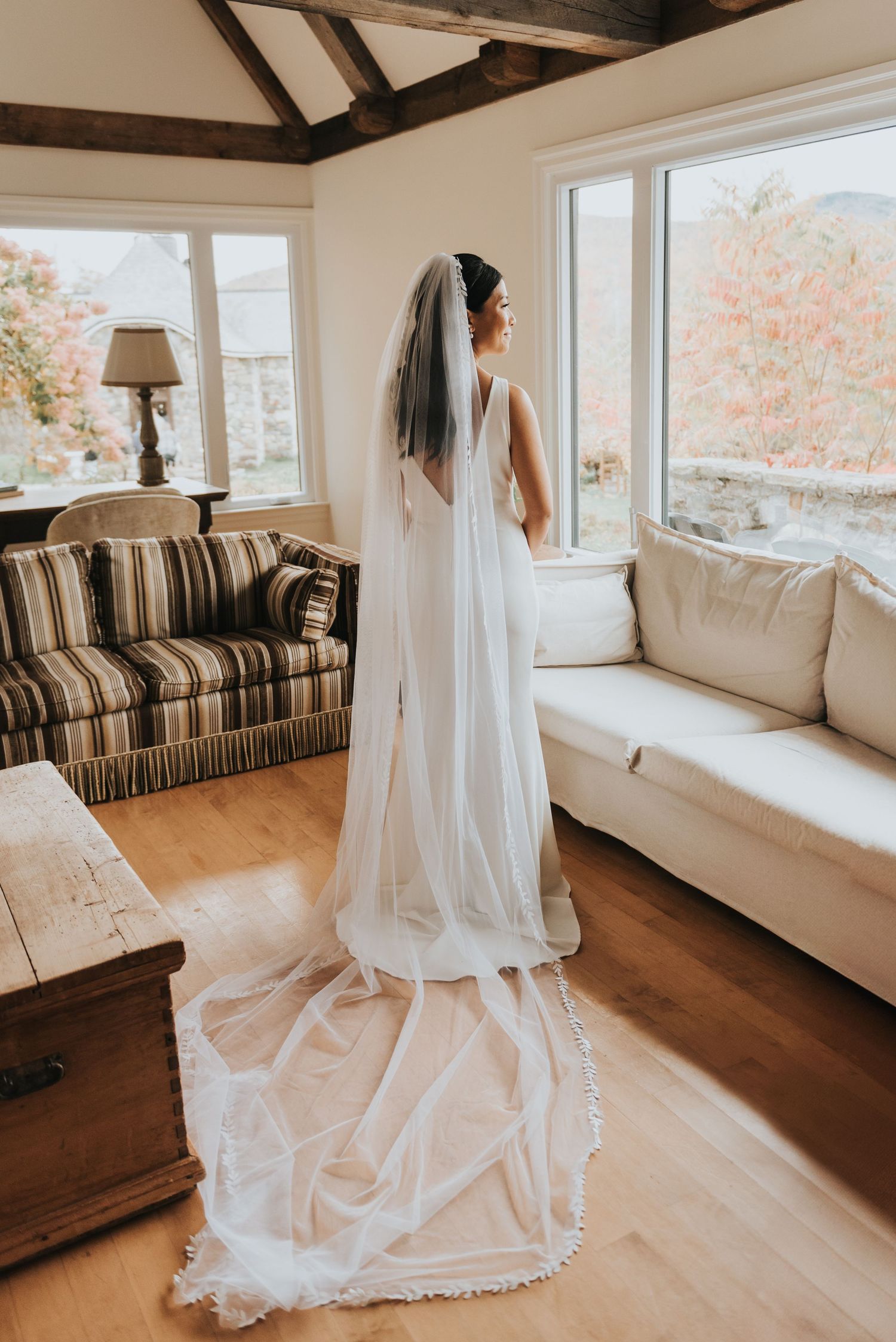 A flowing cathedral-length lace wedding veil drapes elegantly in a sunlit room with autumn views.