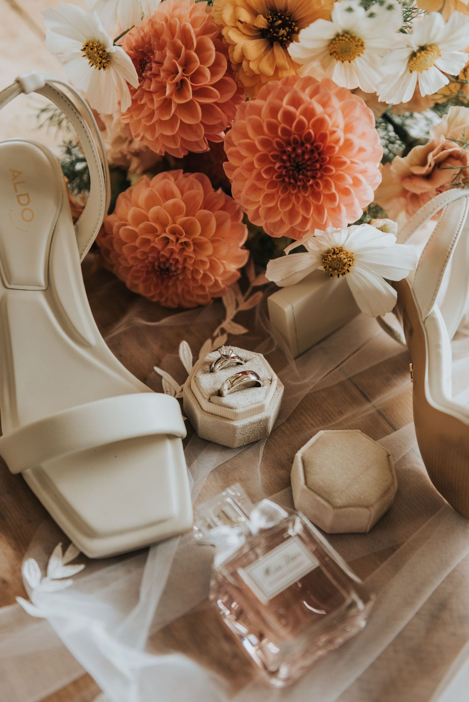 Elegant wedding details featuring coral dahlias and white daisies arranged with white high heel shoes.