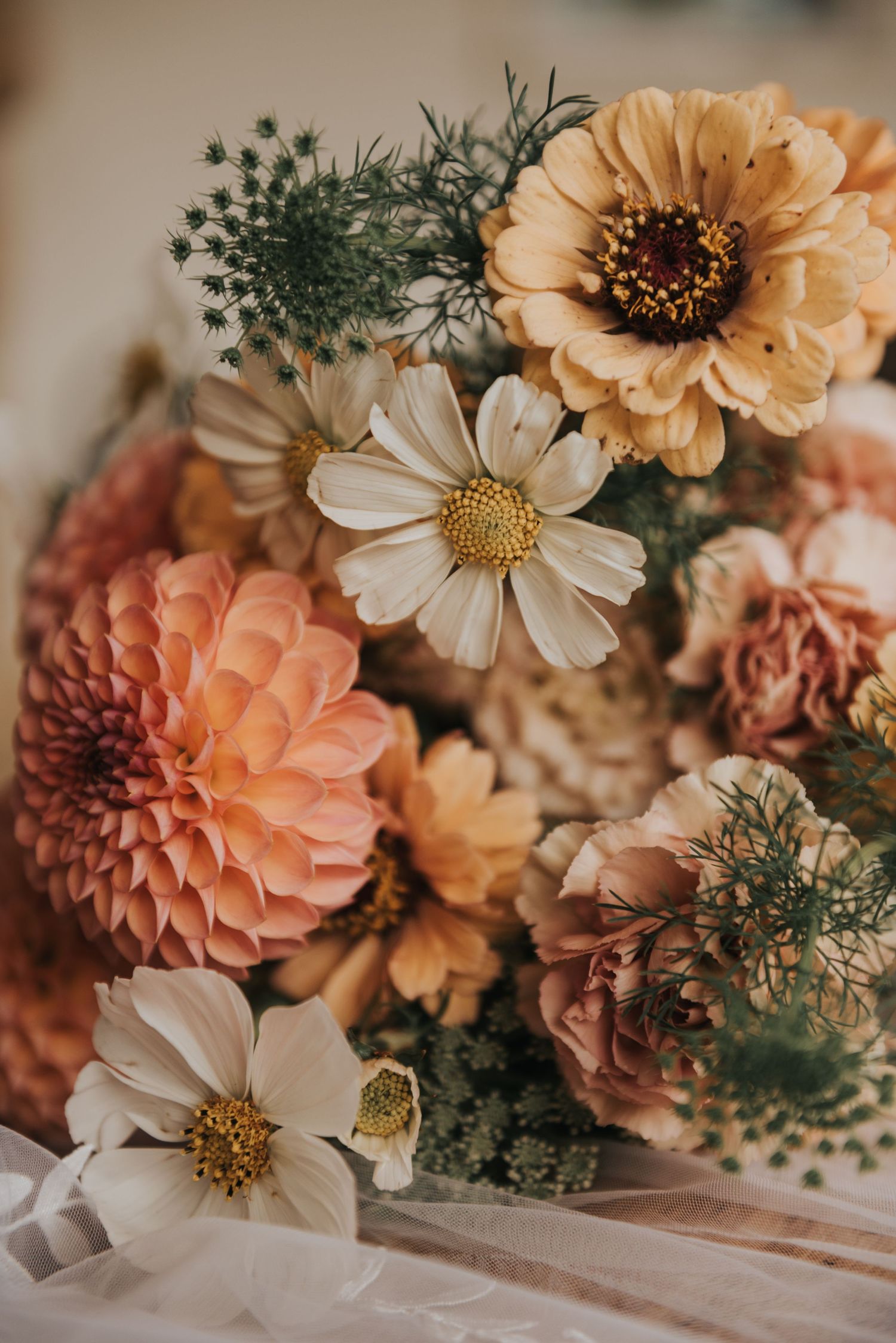 Close-up of a romantic floral arrangement with peach dahlias, white daisies, and delicate greenery.