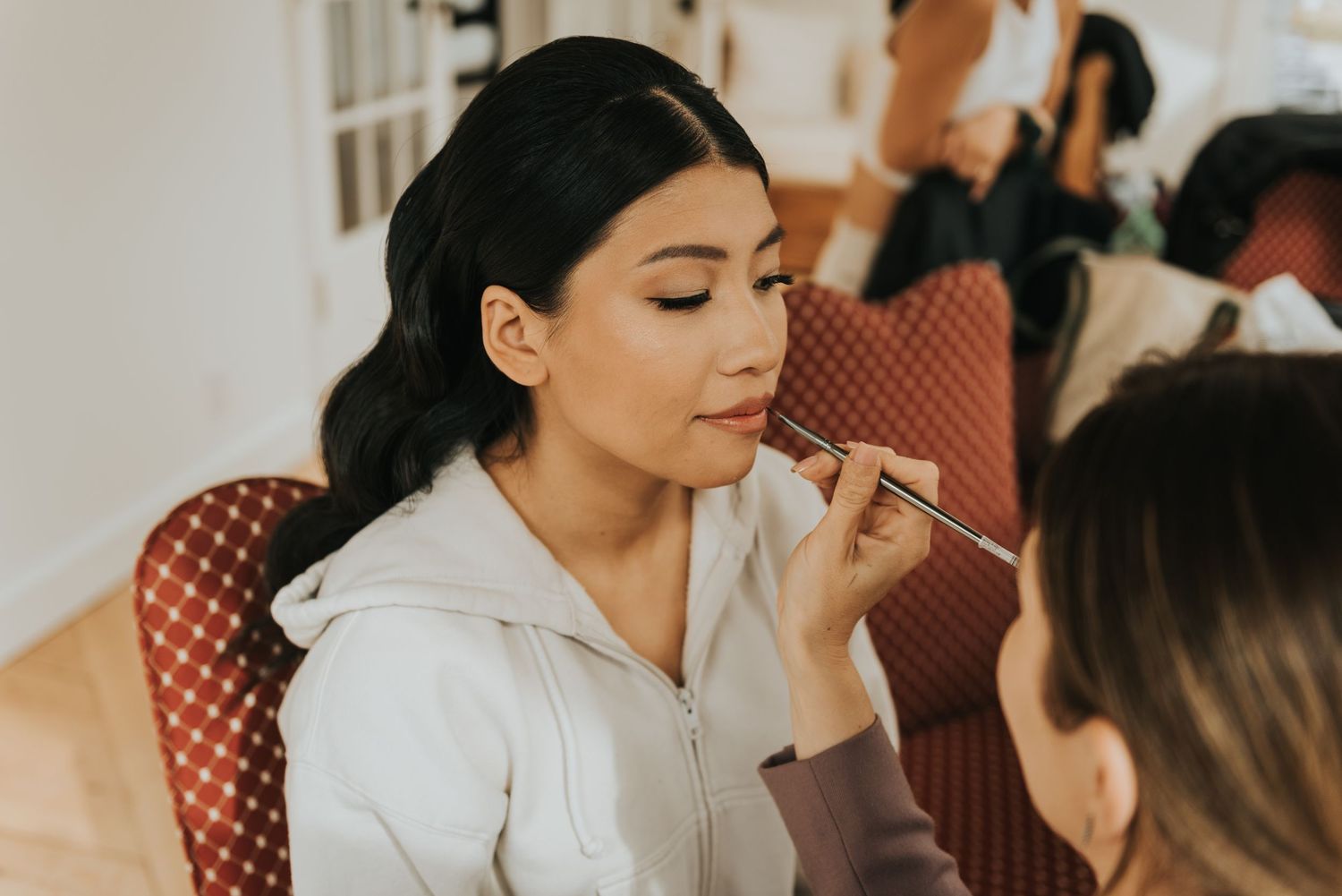 Makeup artist carefully applies makeup to a woman in a white dress before a special event.