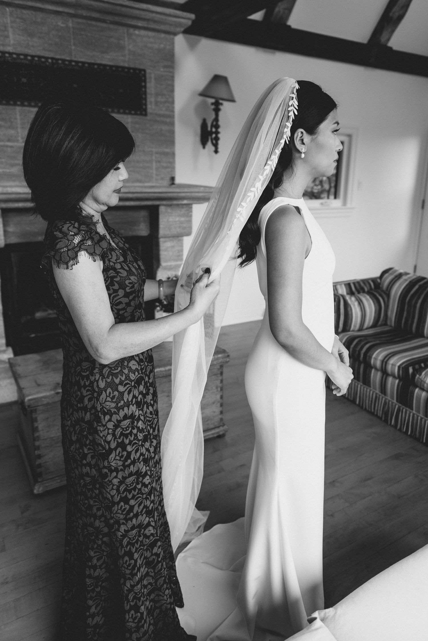 Black and white wedding preparation photos show a moment of dress adjustment between two people in a dimly lit room.