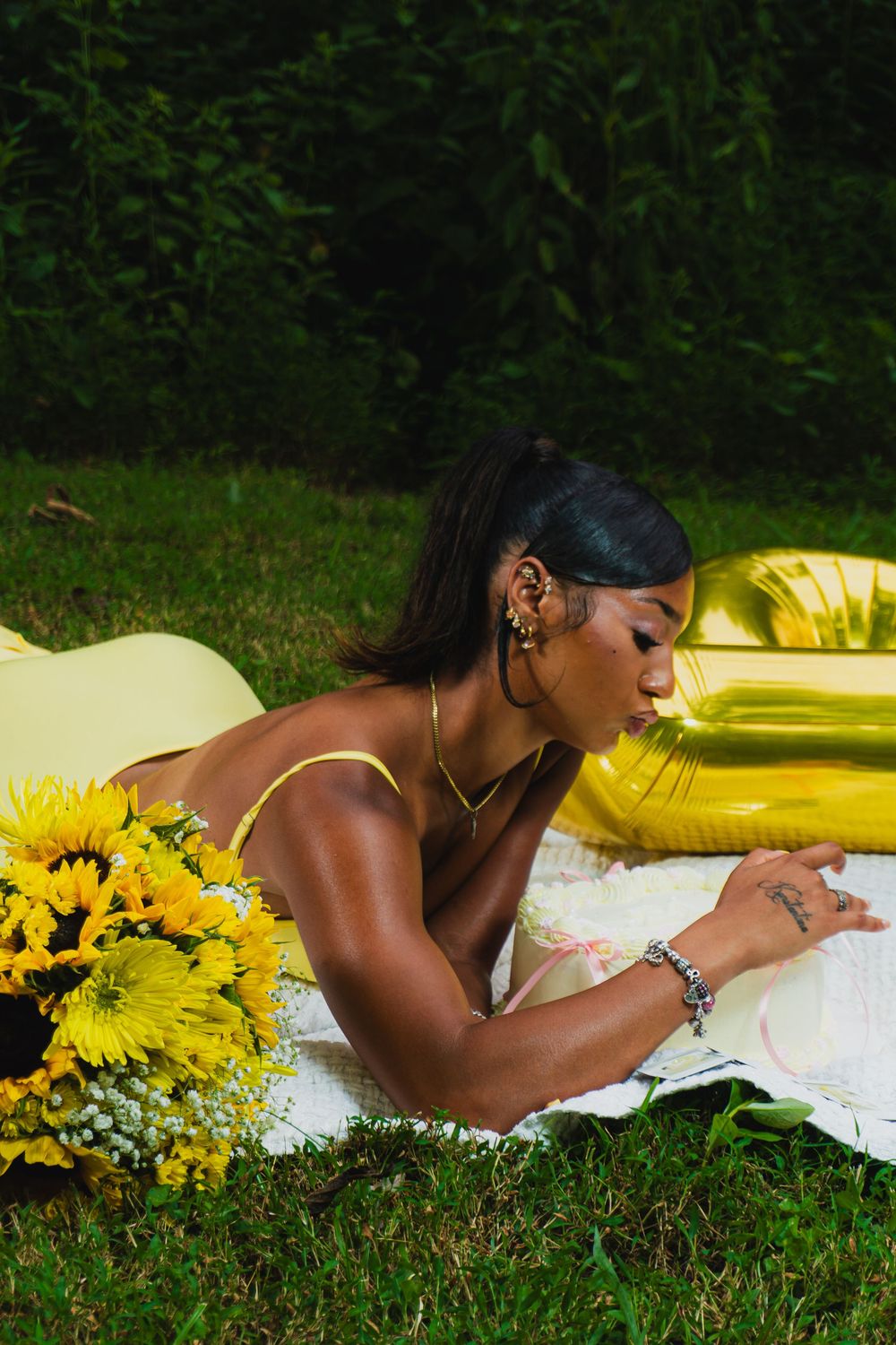 Outdoor photo featuring yellow dress and sunflower arrangements on white blanket.