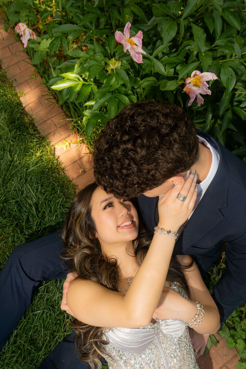 Couple shares intimate moment lying among pink flowers in garden setting.