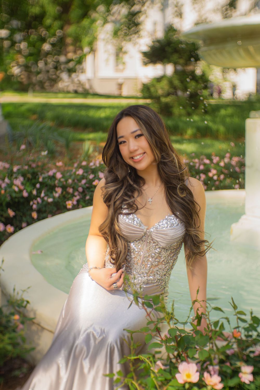 Romantic garden photoshoot featuring an embellished silver gown near blooming flowers and a water feature.