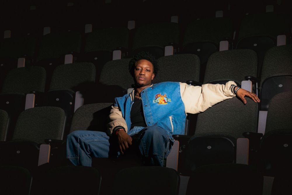 Person in retro varsity jacket lounging in dark theater seating.