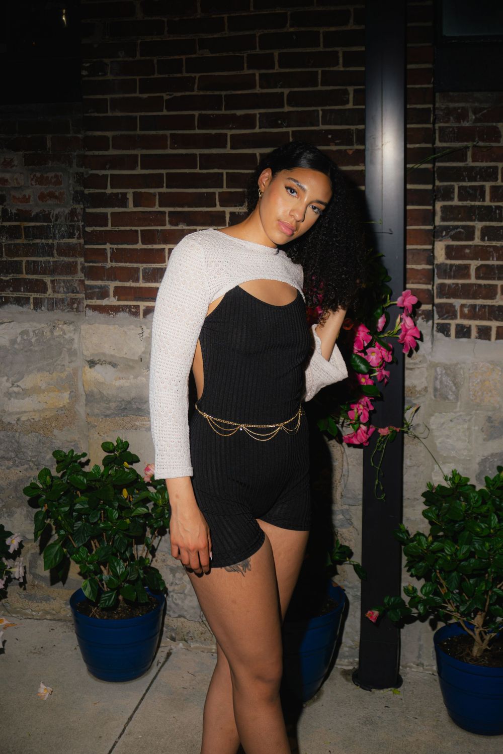 Stylish pose against brick wall with blue planters and pink flowers.