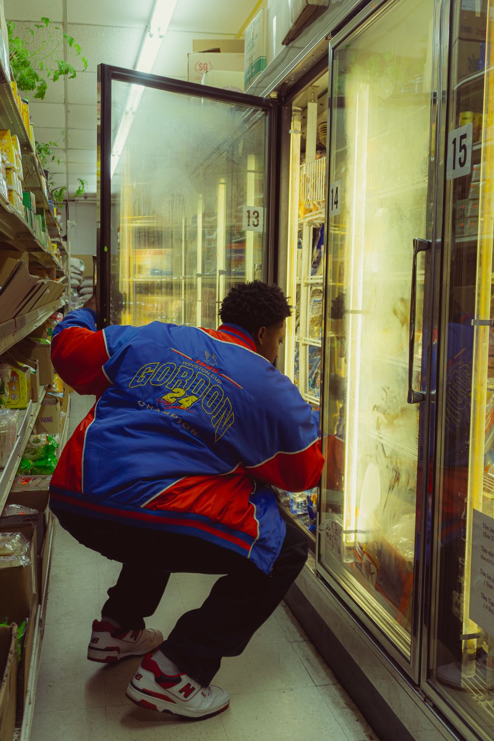Person in blue and red uniform bends down to check items in a commercial freezer aisle.