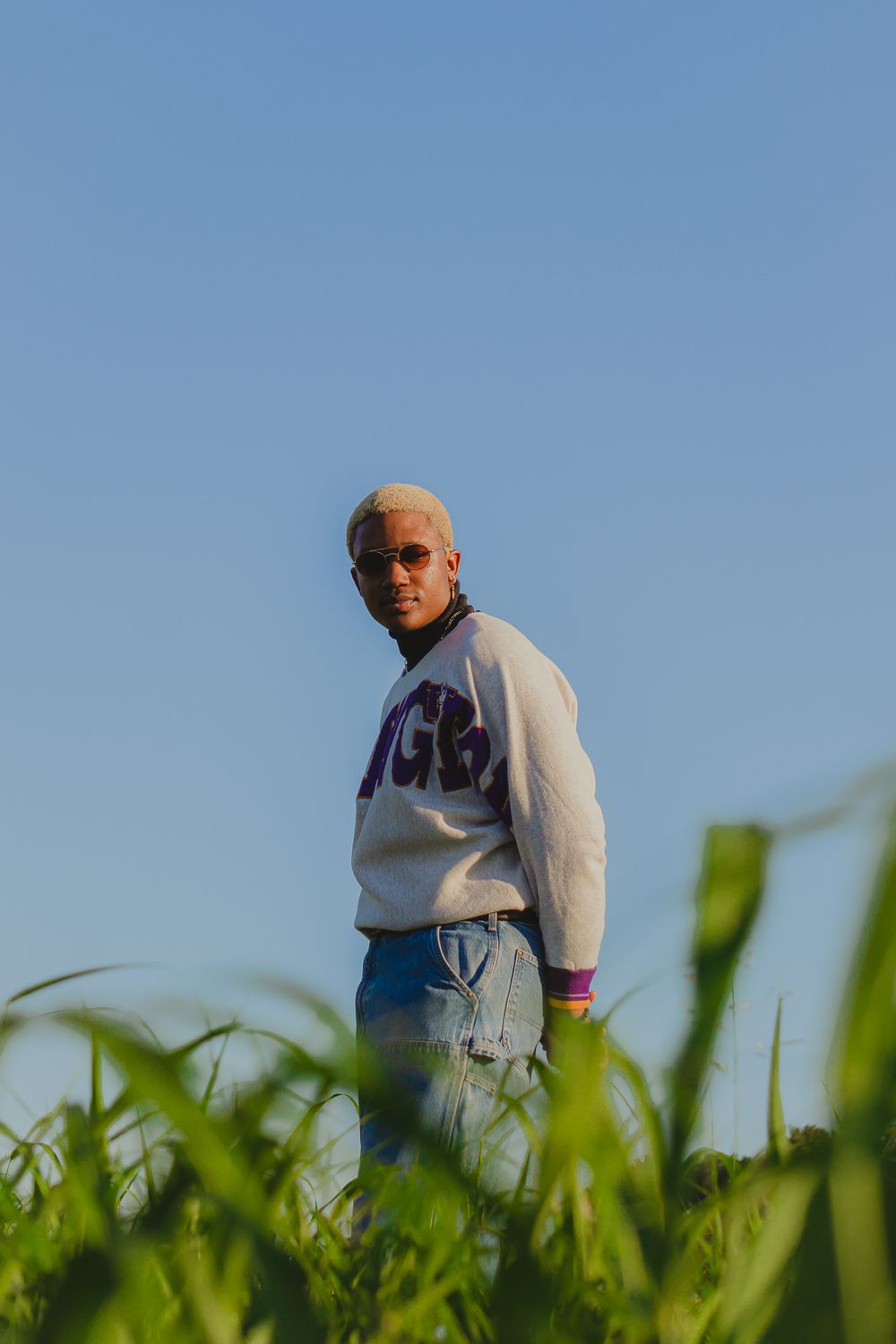 Figure in white sweatshirt photographed against blue sky and green grass.