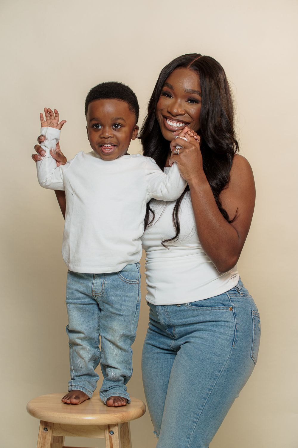A joyful pair in matching white tops and blue jeans share playful moments while posing on a wooden stool.