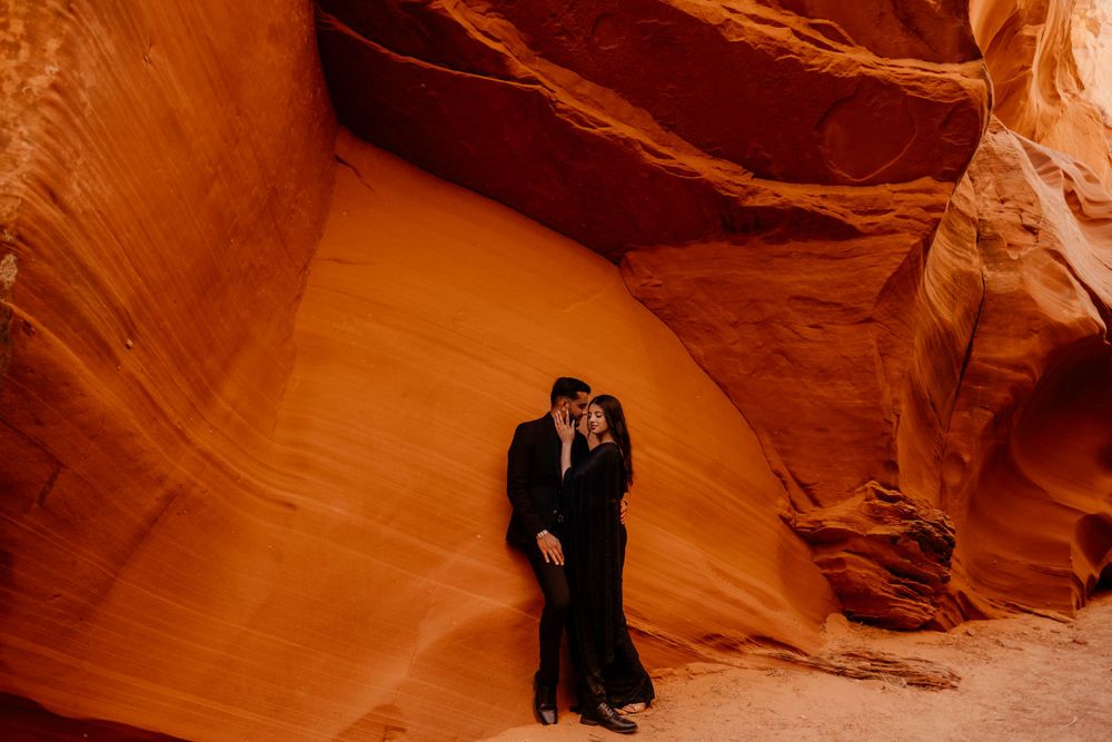 A couple in formal attire embraces while standing in a dramatic orange slot canyon with towering sandstone walls.