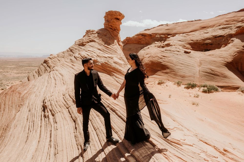 Two people pose dramatically on smooth sandstone formations in the desert landscape.