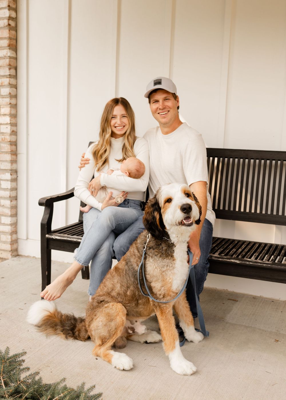 Family sitting on a black bench on porch with a large brown and white Saint Bernard dog.
