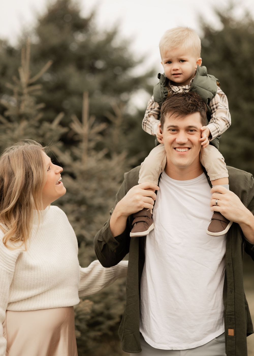 Family shares joyful moment together at Christmas tree farm on autumn day with pine trees in background.