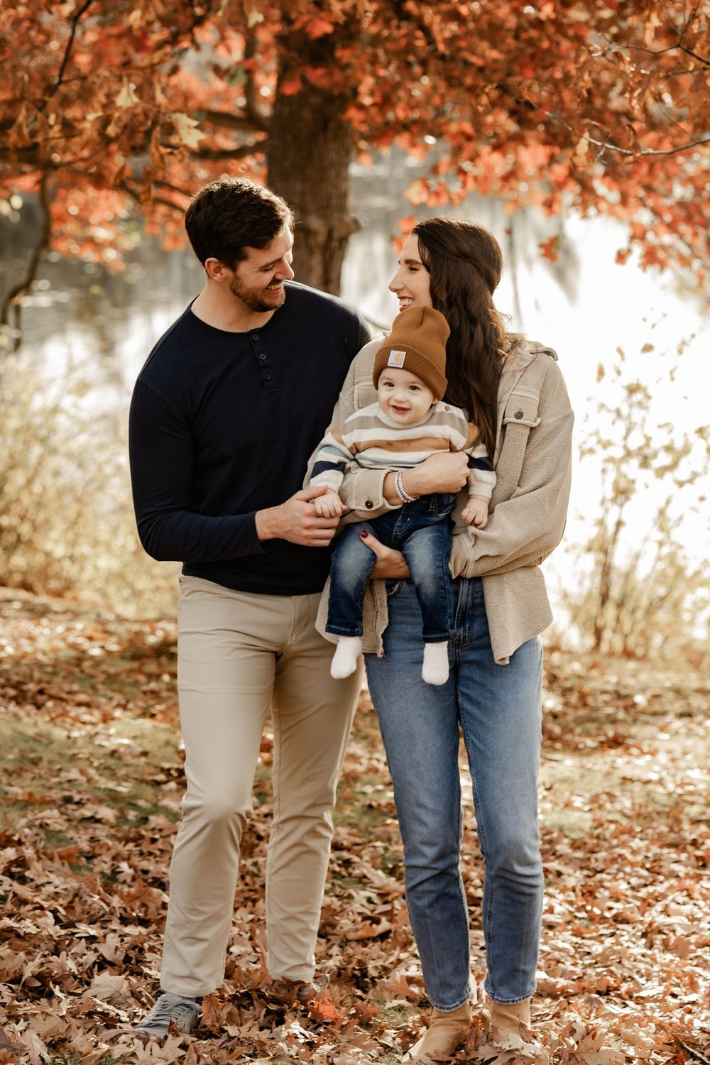 A family poses together in a fall setting with autumn leaves and warm colors creating a cozy outdoor portrait.