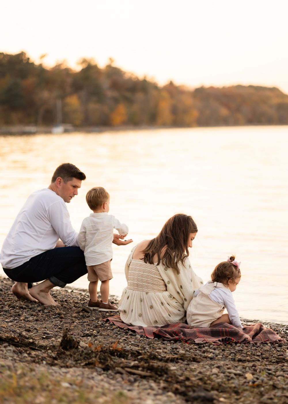 Family spends peaceful evening by lake shore during golden sunset as they sit together on rocky beach.