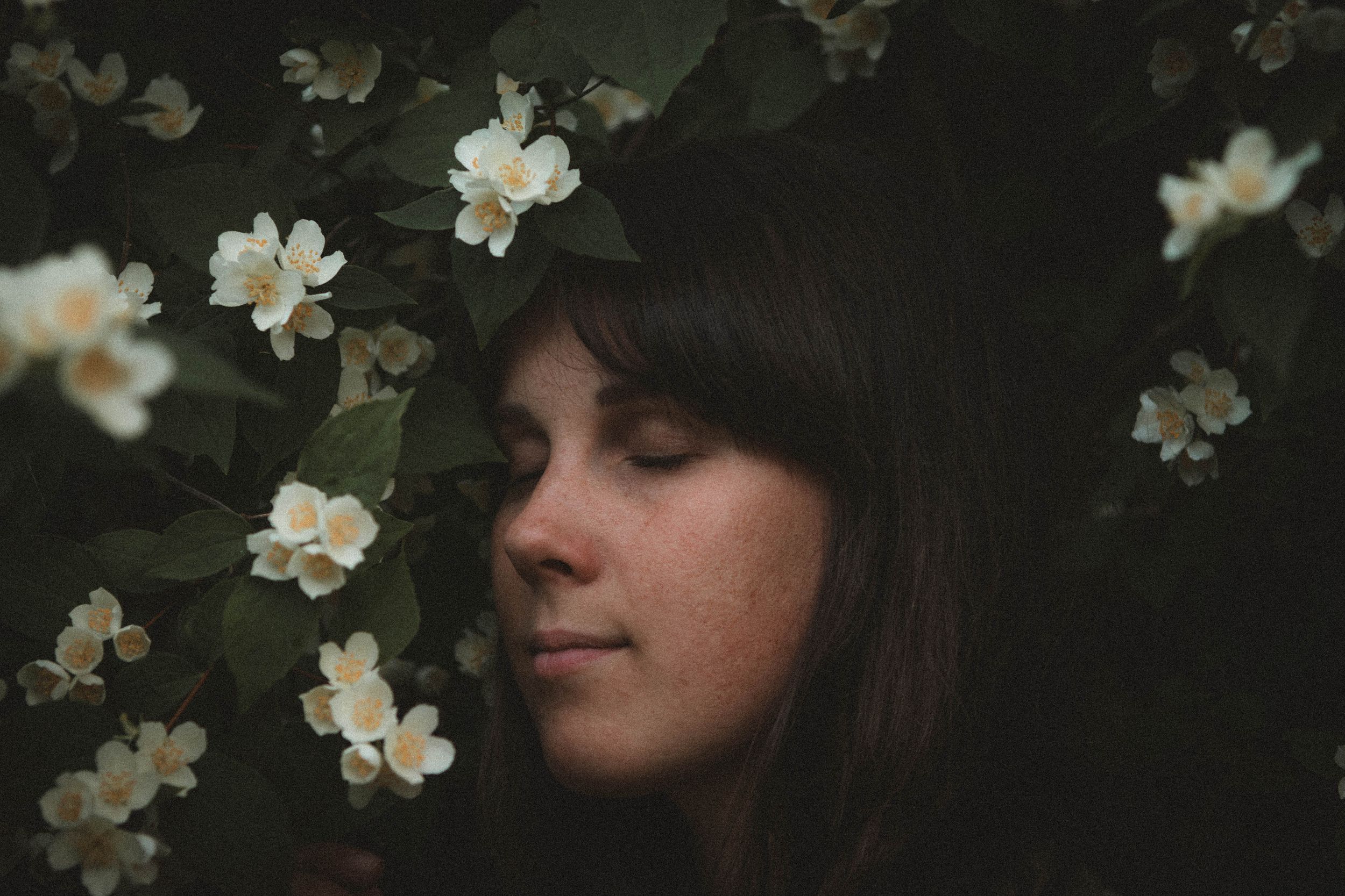 Artistic moody portrait surrounded by delicate white jasmine flowers in a dark garden setting.