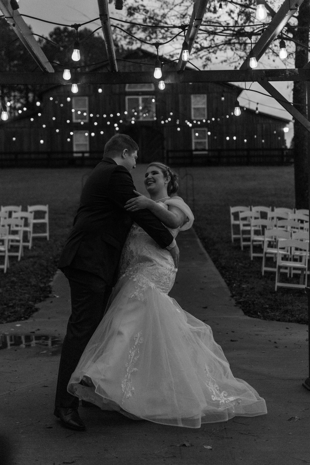 A romantic black and white dance sequence at an outdoor wedding reception with string lights overhead.