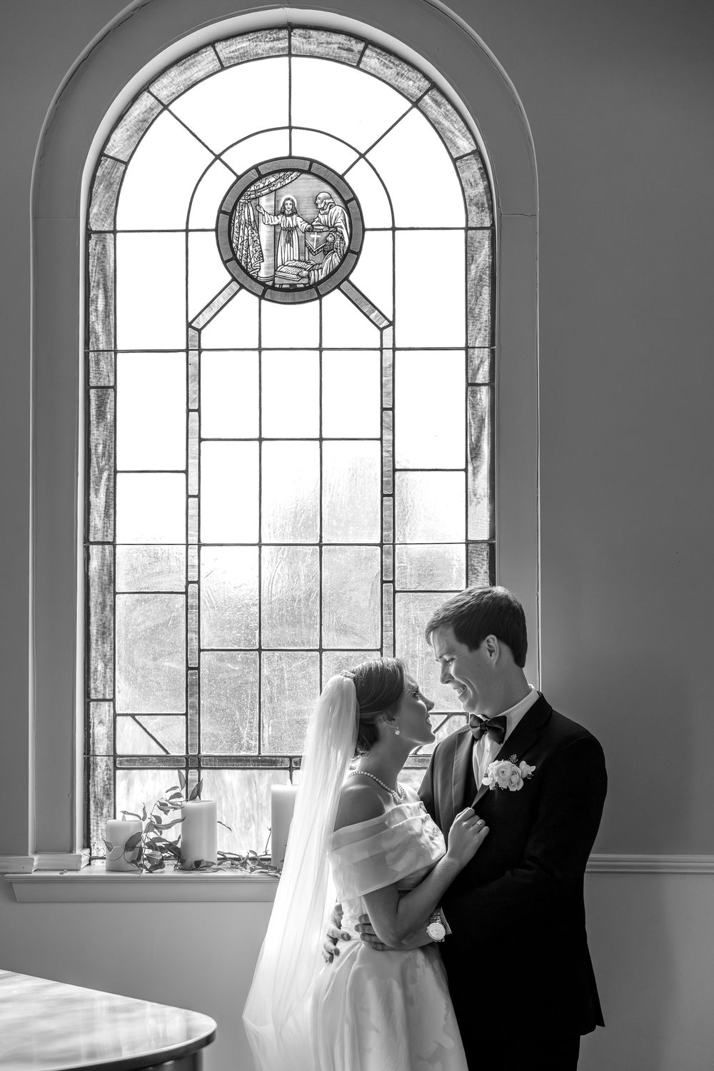 Wedding couple dancing in elegant church setting with arched stained glass windows.