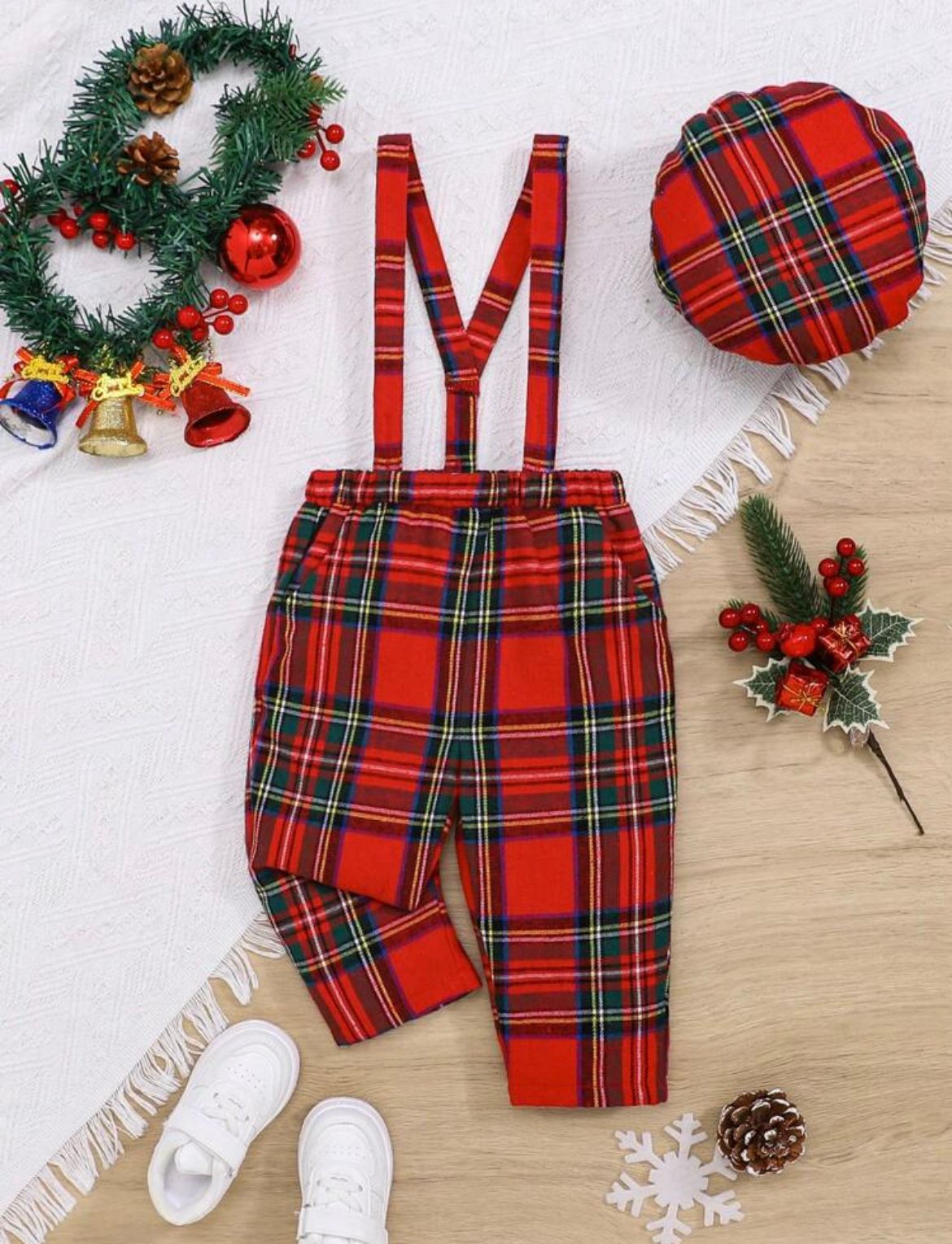 Red plaid Christmas outfit with suspenders and decorative holiday elements on wooden surface.