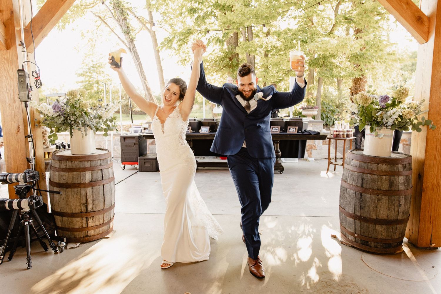 Newlyweds celebrate with raised arms in a rustic barn venue decorated with wooden barrels.