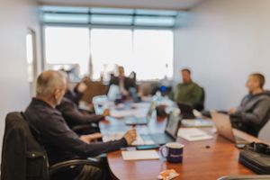 Business professionals gathered around a conference table in a bright office meeting room during a presentation.