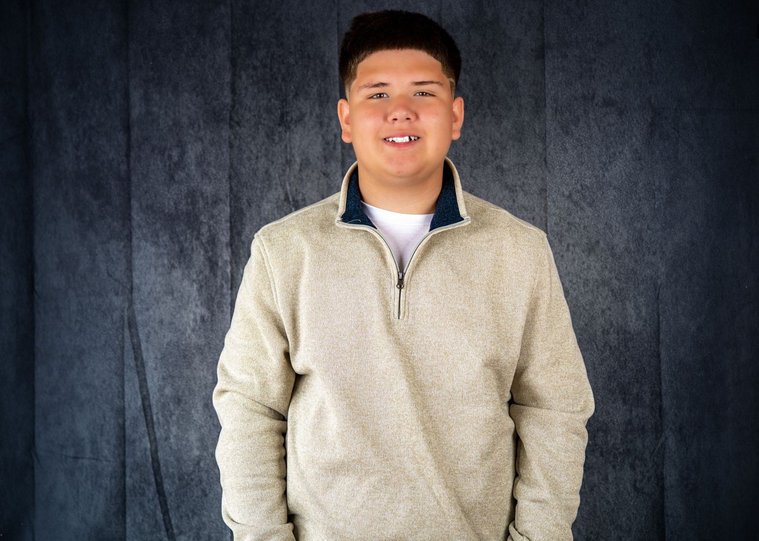 Portrait of a person wearing a light colored pullover against a dark textured background.