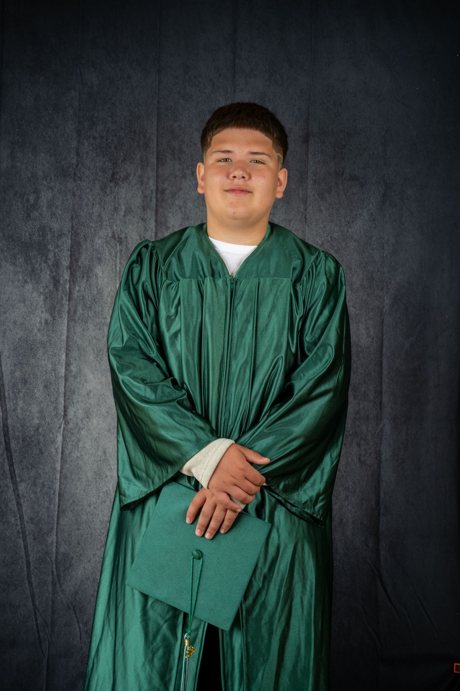 A graduate poses in traditional green academic regalia against a dark background.