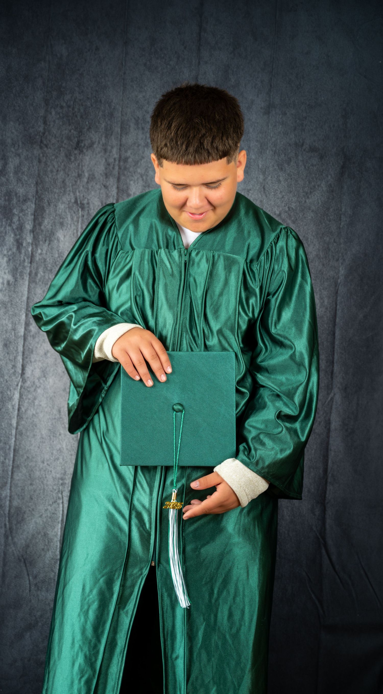 Person in emerald green graduation gown demonstrating how to unzip and open the robe for wearing.