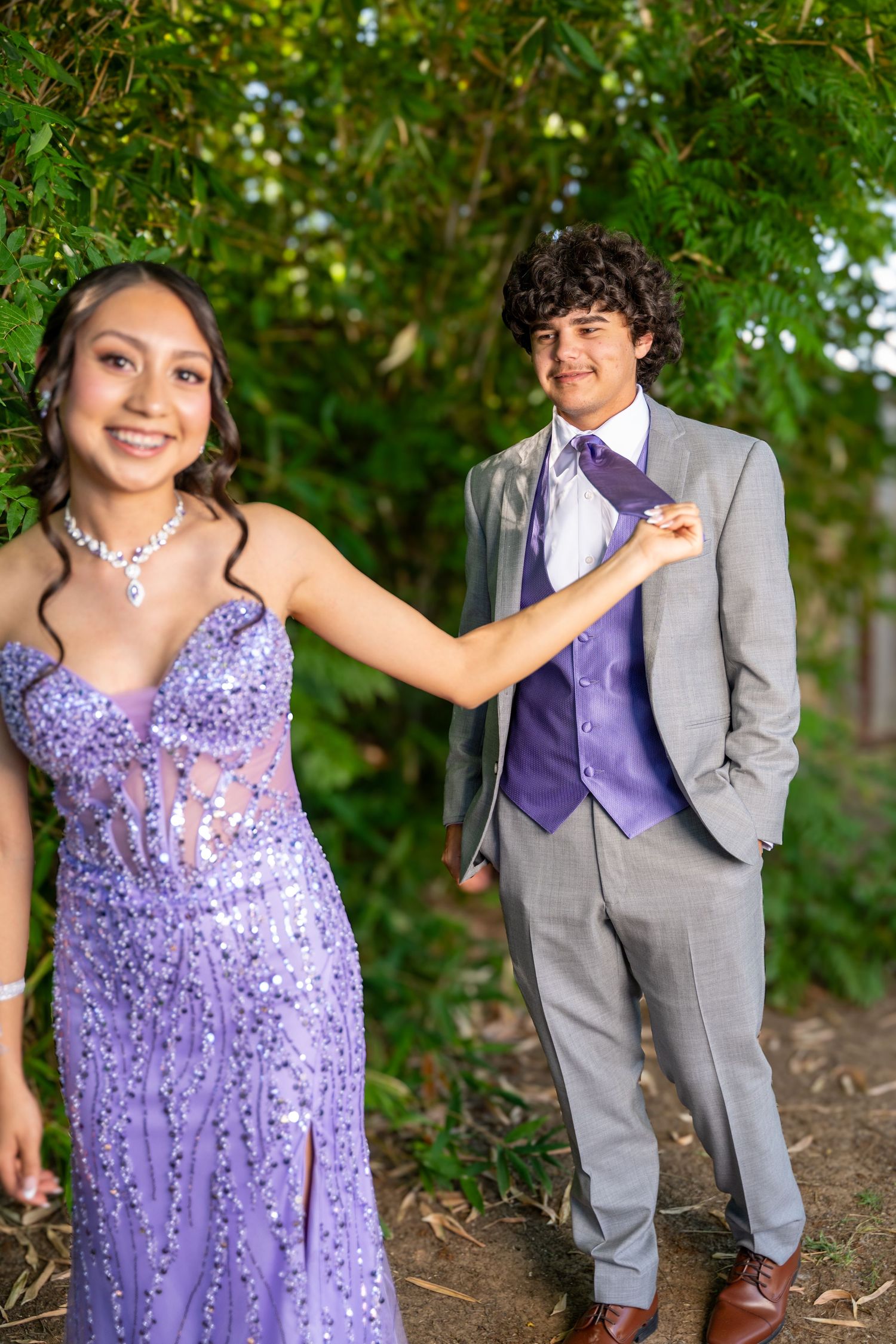 Prom couple in purple and grey formal attire pose in garden setting.
