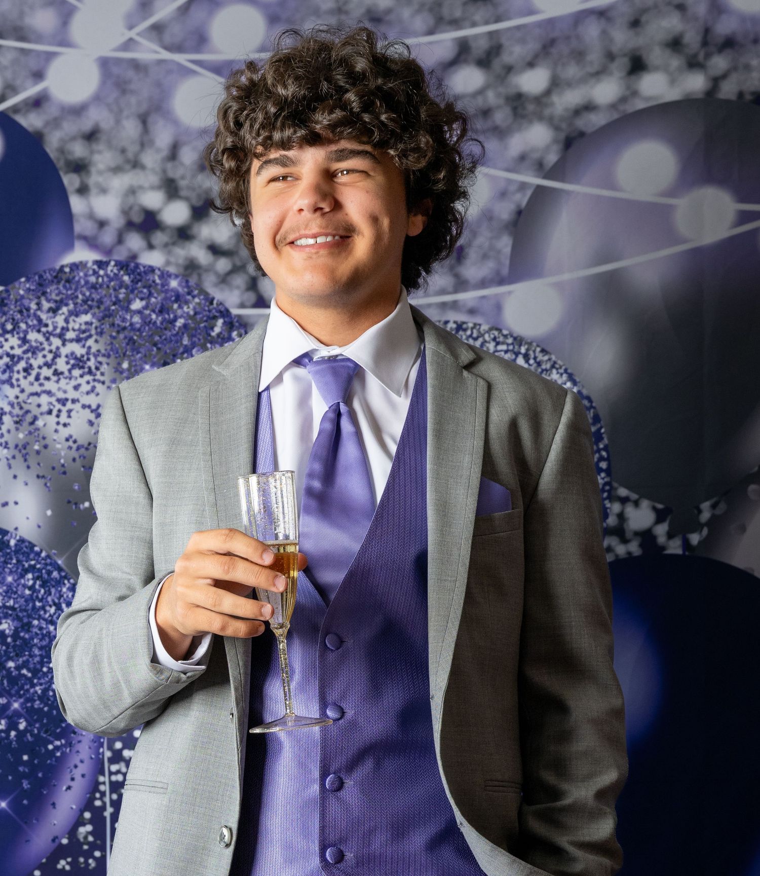 Formal event attendee in grey suit and purple tie holds champagne glass.