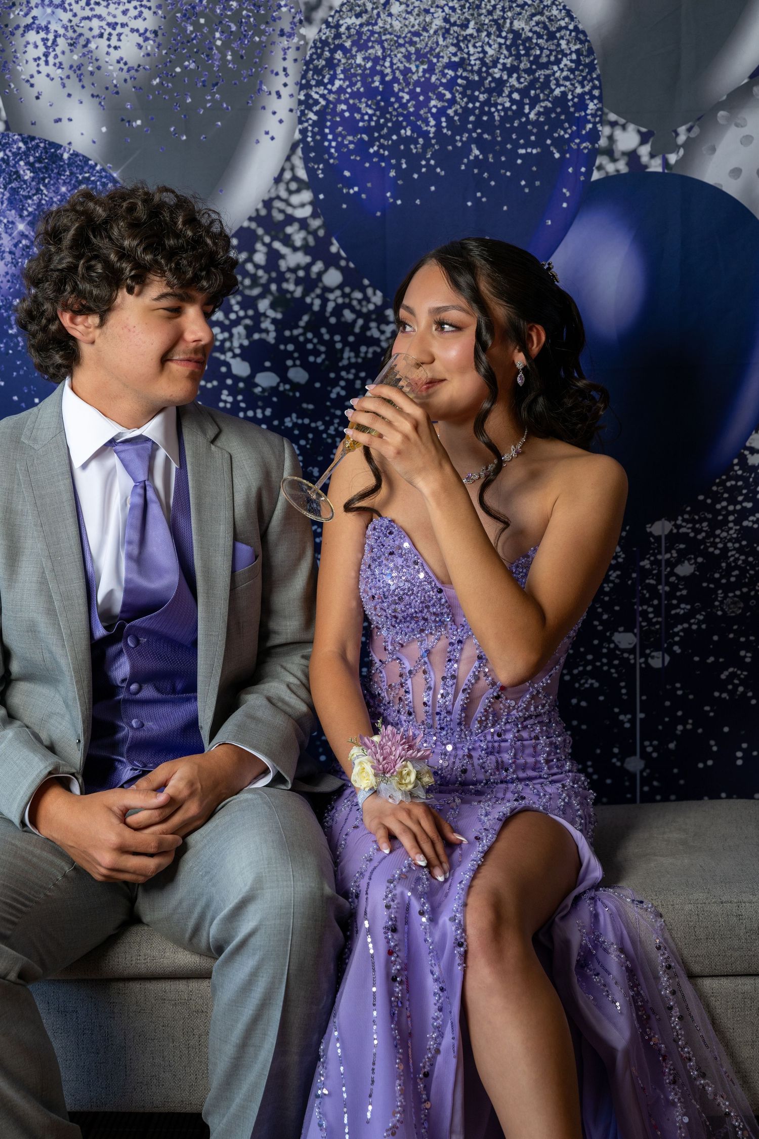 Formal couple in purple and grey attire sit together against sparkly backdrop.