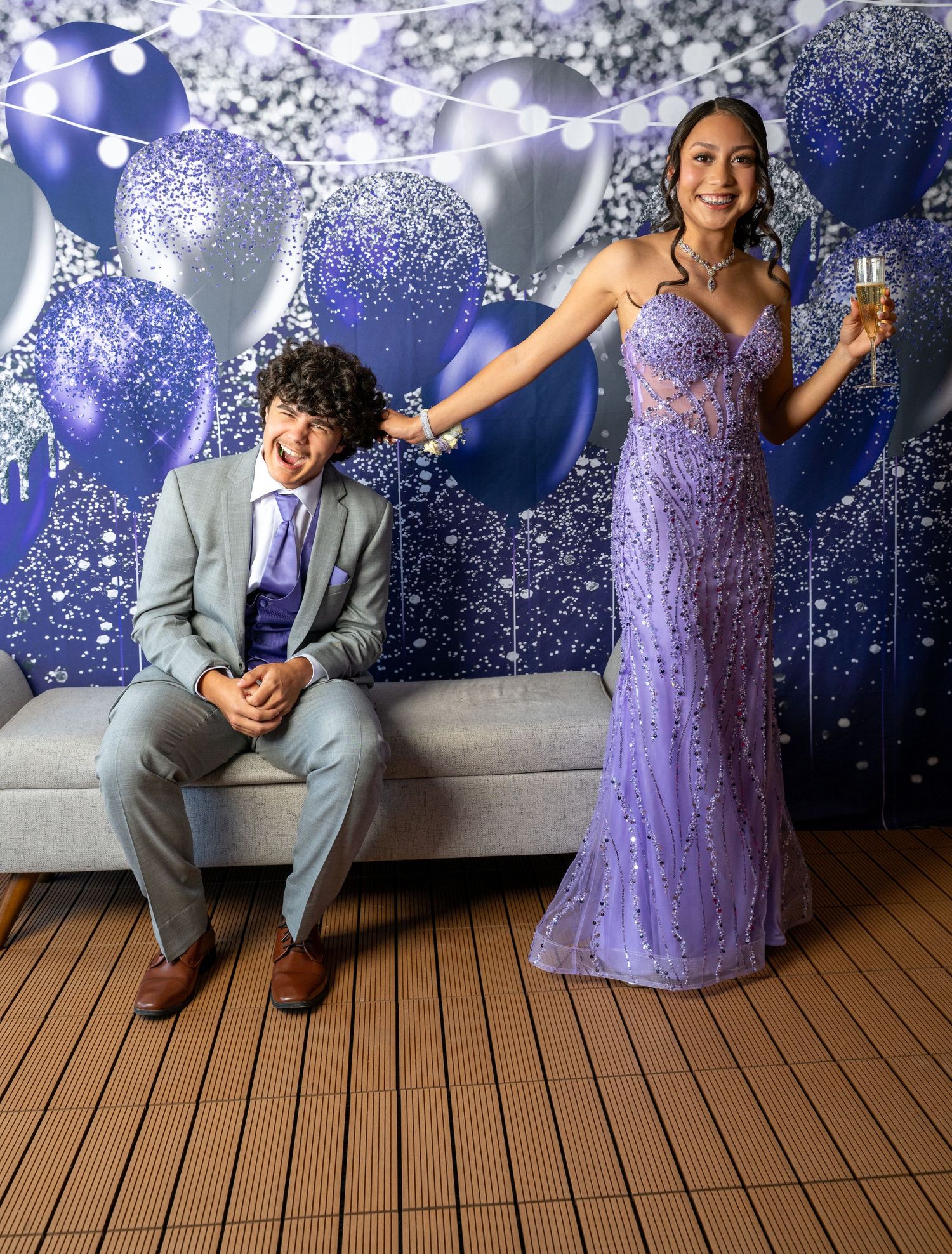A couple poses together for prom or formal event photos against a sparkly blue backdrop with string lights.