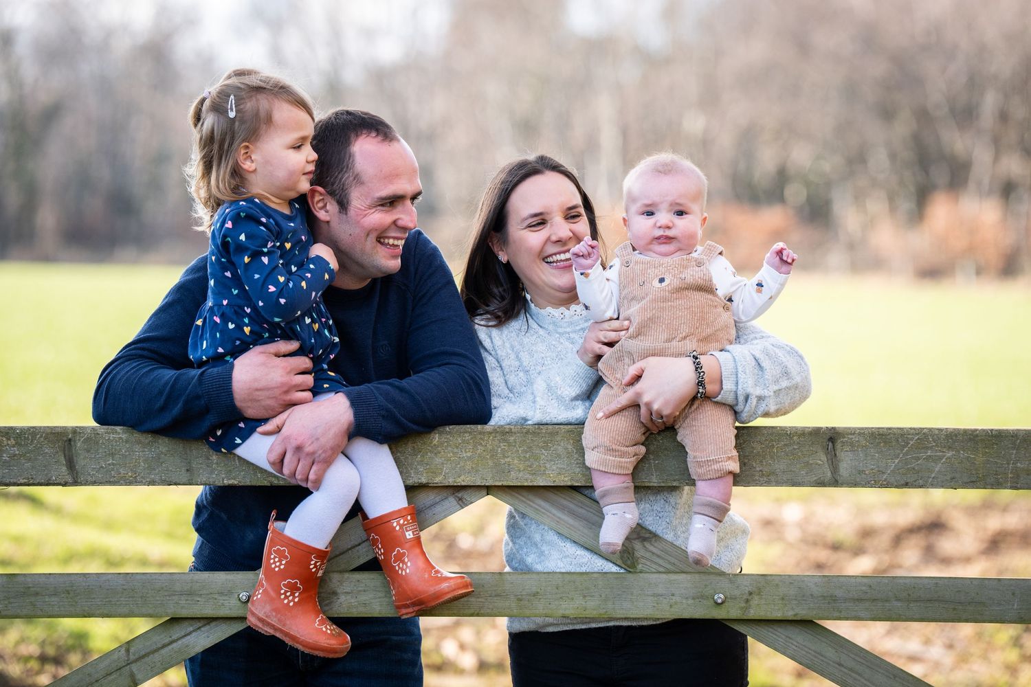 Family sitting together on wooden fence enjoying a casual outdoor photo session.