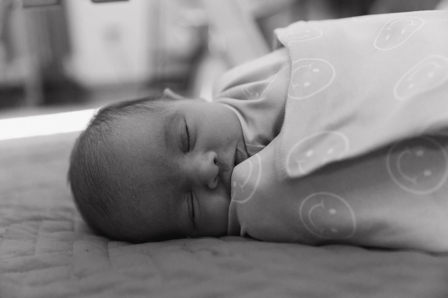 A peaceful newborn baby sleeps soundly in black and white, swaddled in soft white blankets.