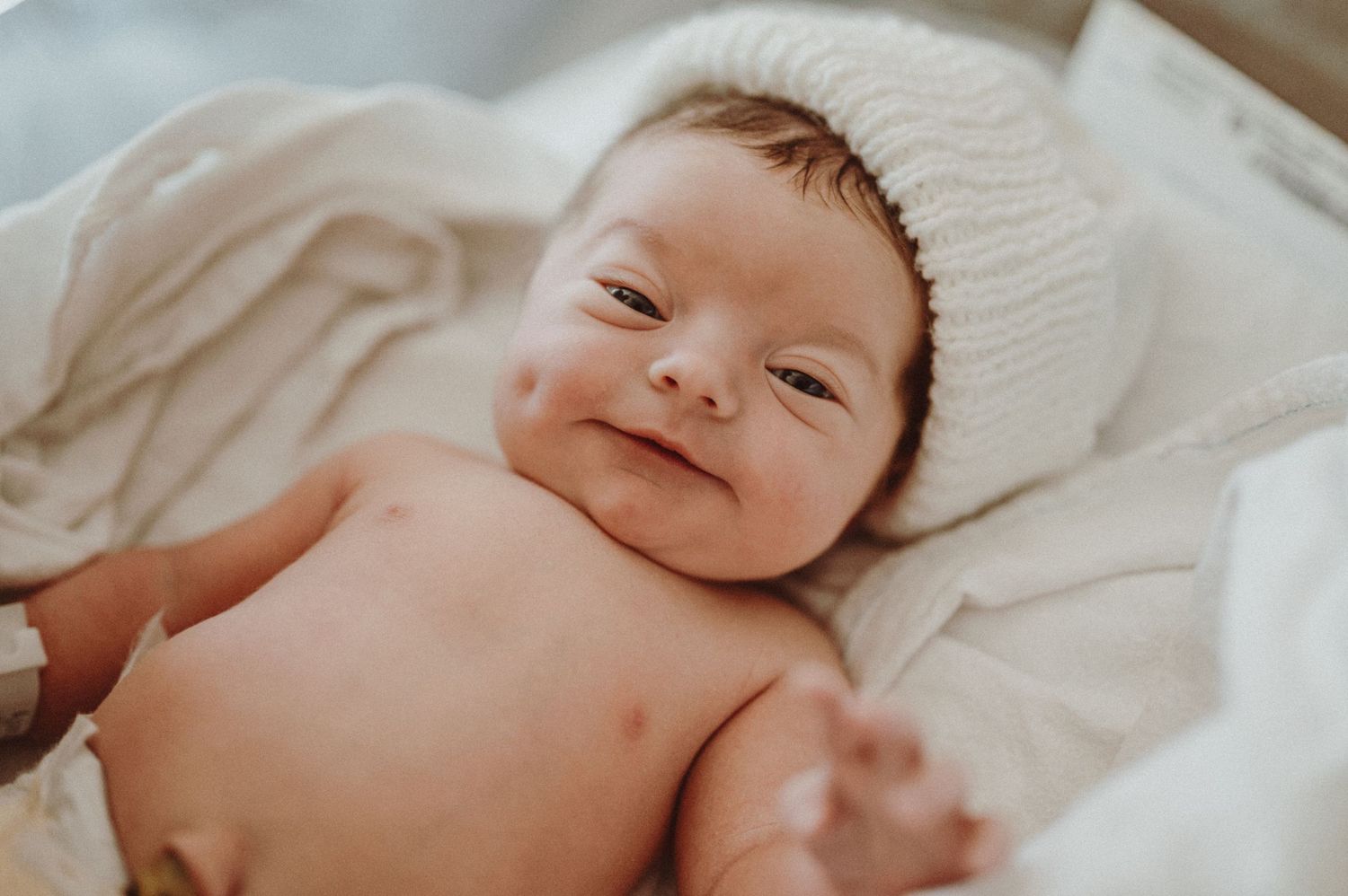 Baby lying on soft white blankets gazes with gentle expression.