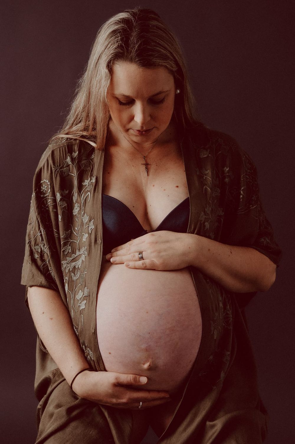 Gravidfotografering i studio. Gravid kvinna håller om sin gravida mage. Hon har en bohemisk kaftan på sig, och en bar mage.