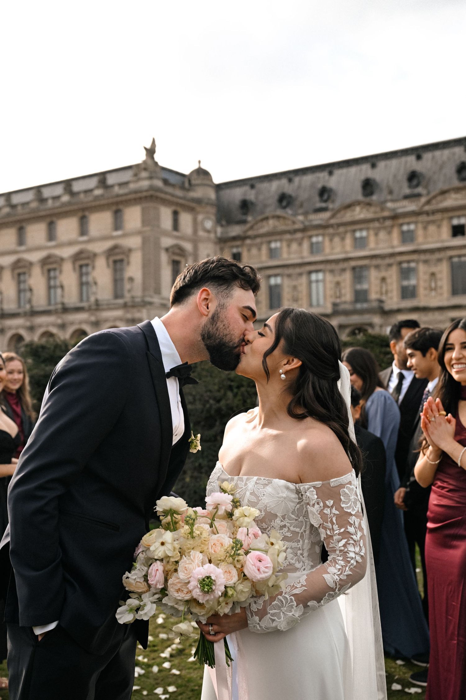 Newlyweds share a kiss during their wedding celebration outside a grand historic palace.