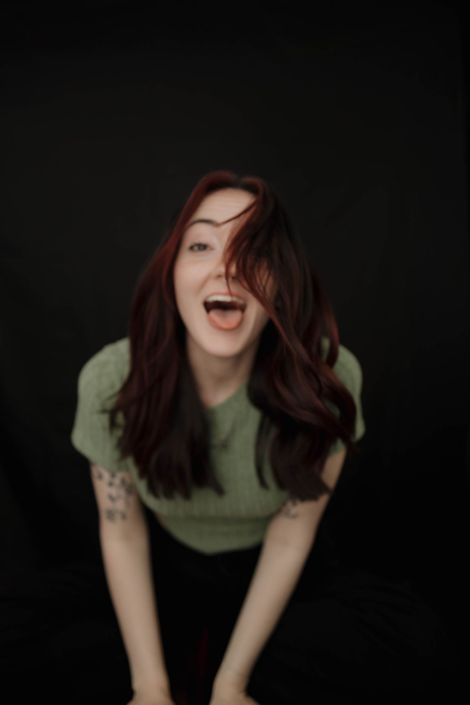 Person in a green t-shirt laughs joyfully with flowing dark hair against a black background.