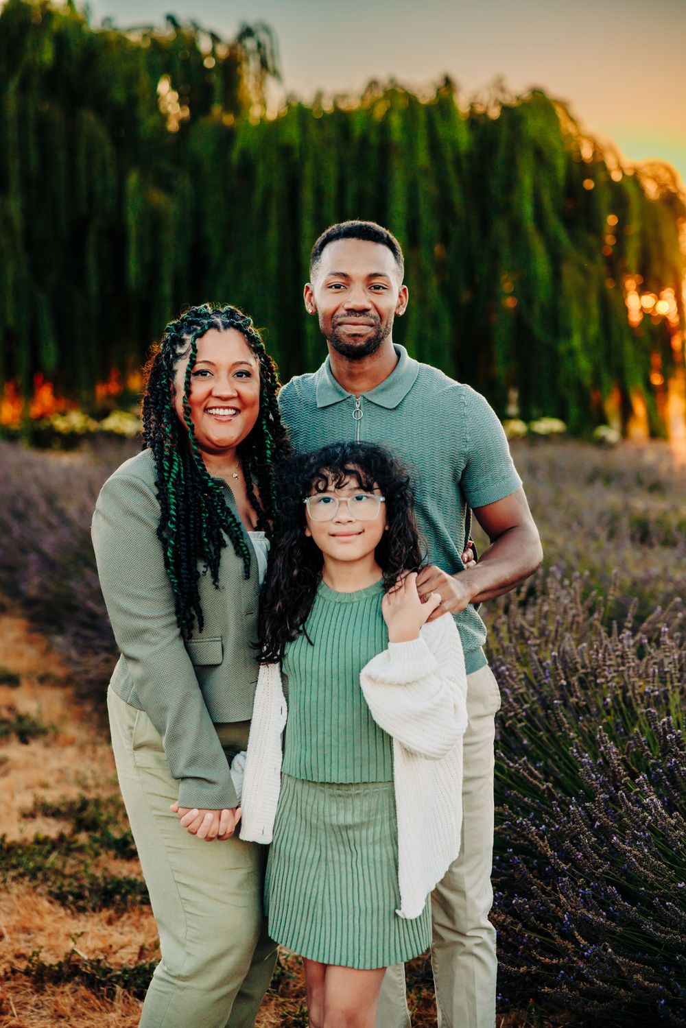 A family poses together at sunset in a lavender field with willow trees in the background.
