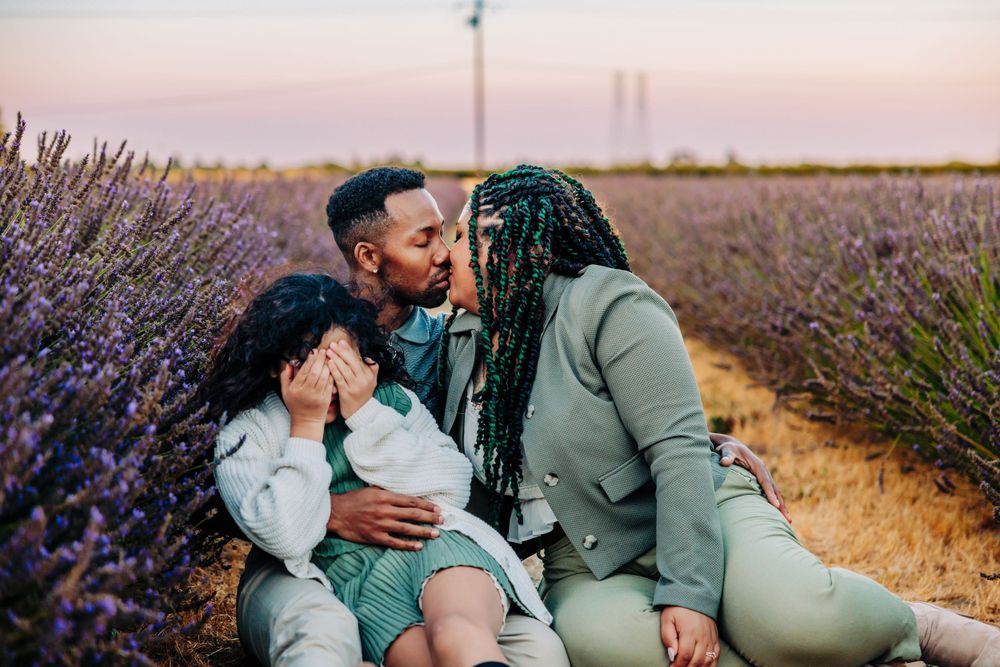 A family shares an intimate moment together while sitting in a blooming lavender field at sunset.