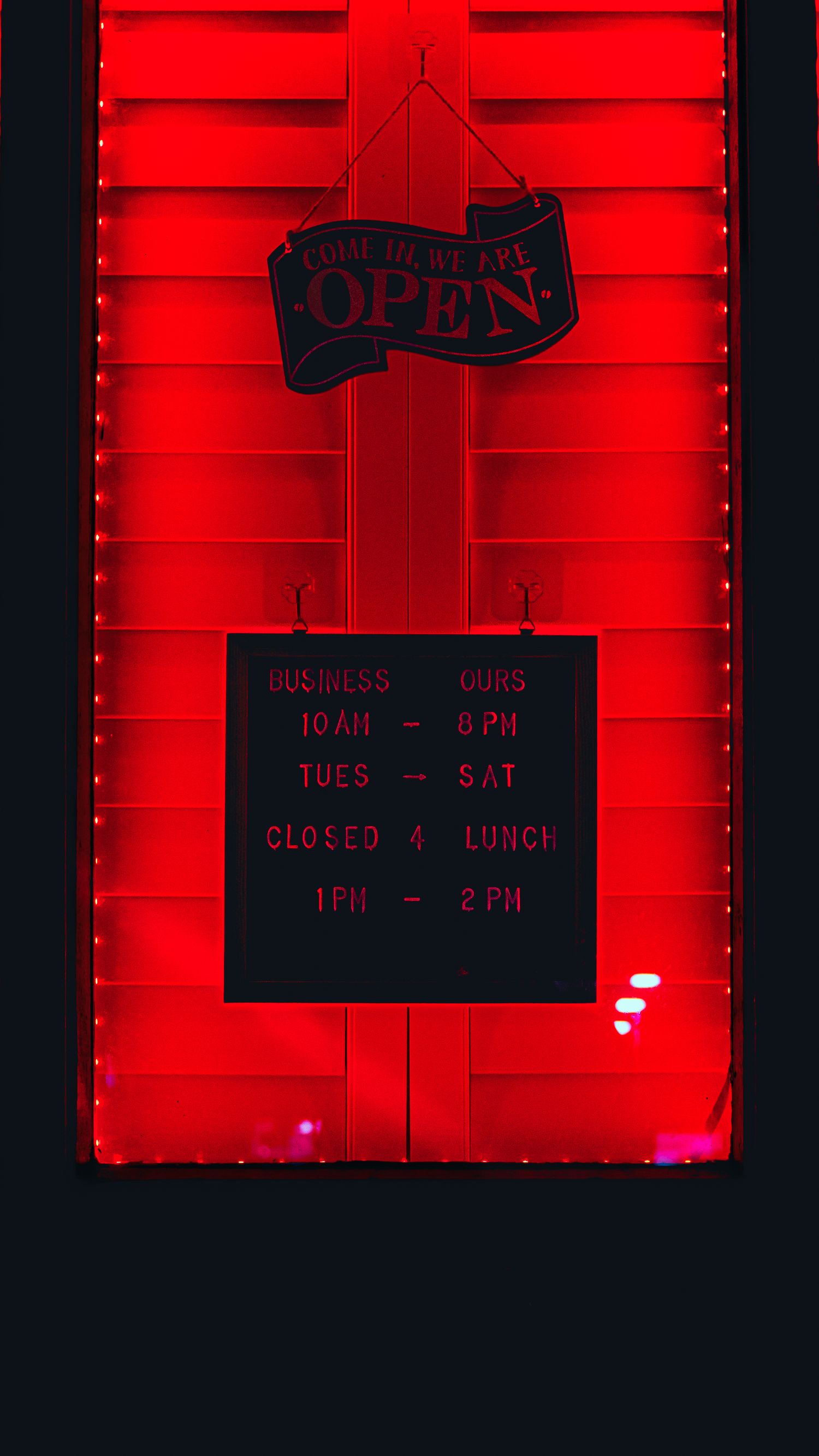 A business hours sign with 'OPEN' text illuminated in red neon lighting on a dark background shows operating times.