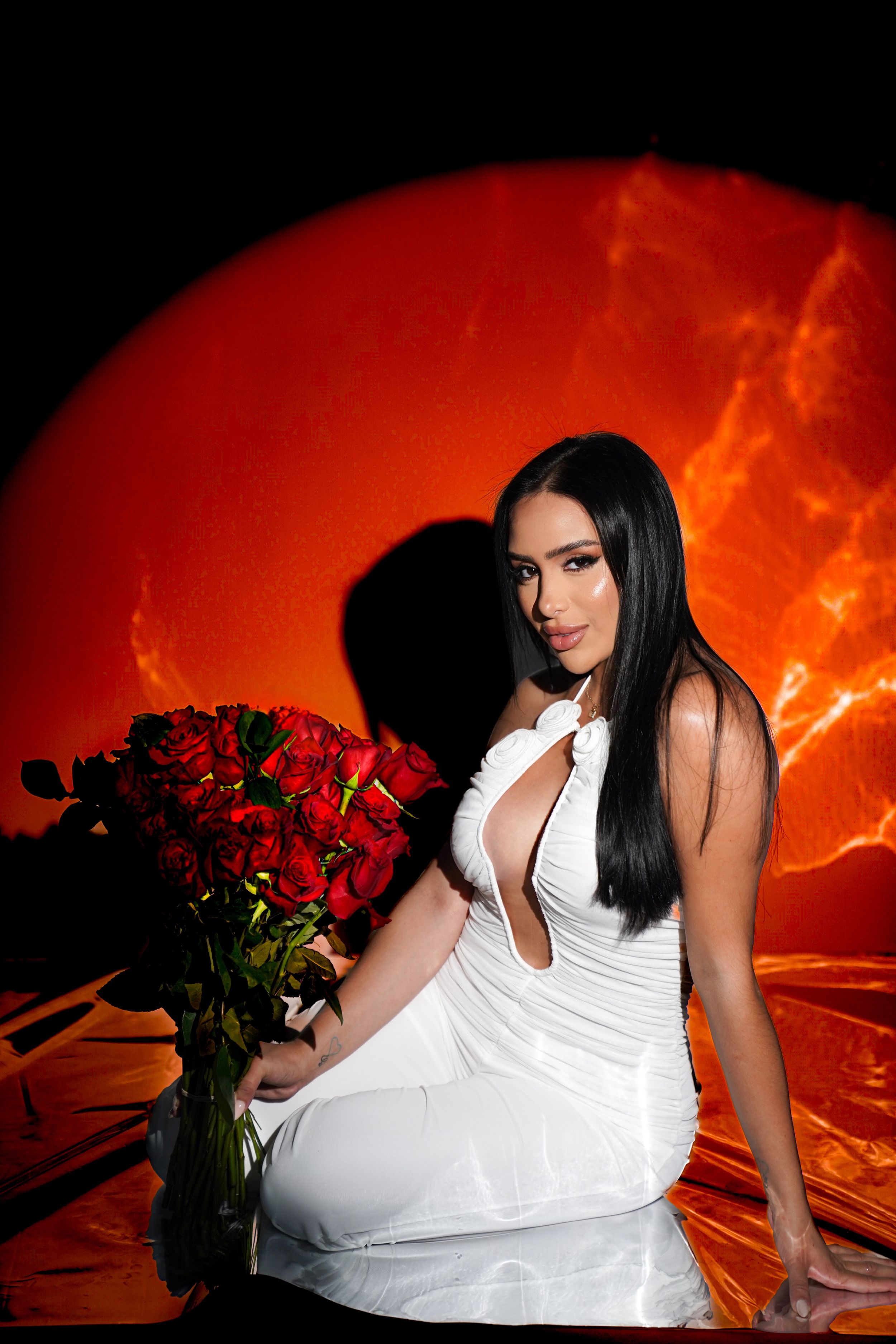 Fashion portraits against fiery orange background featuring white dress and red roses.