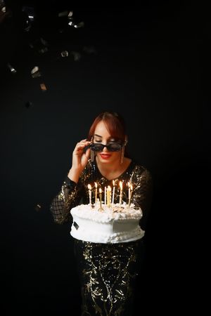 Moody portrait with birthday cake and lit candles against dark background.