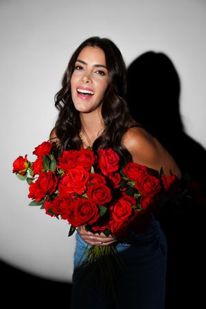Fashion portrait with vibrant red roses against stark white background and dramatic shadows.