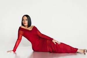 Model in red evening gown poses elegantly in studio against white backdrop.