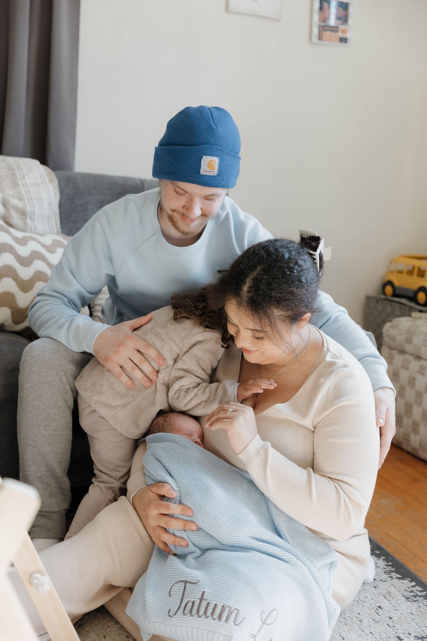 A tender family moment as parents comfort their young child together in a cozy living room setting.