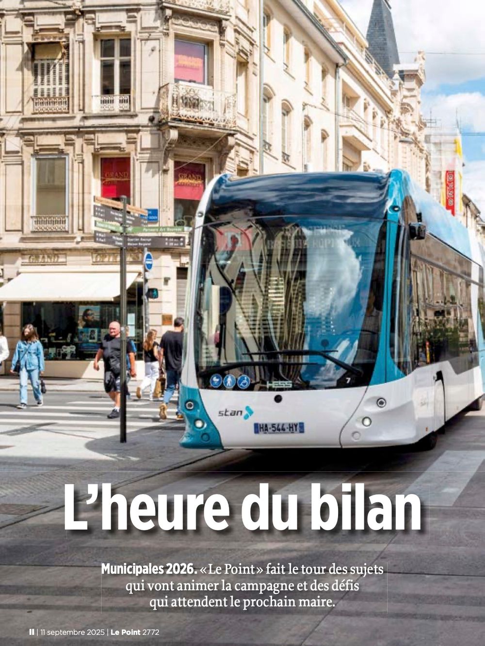 A modern blue and white tram travels through an elegant European city street with historic architecture in the background.